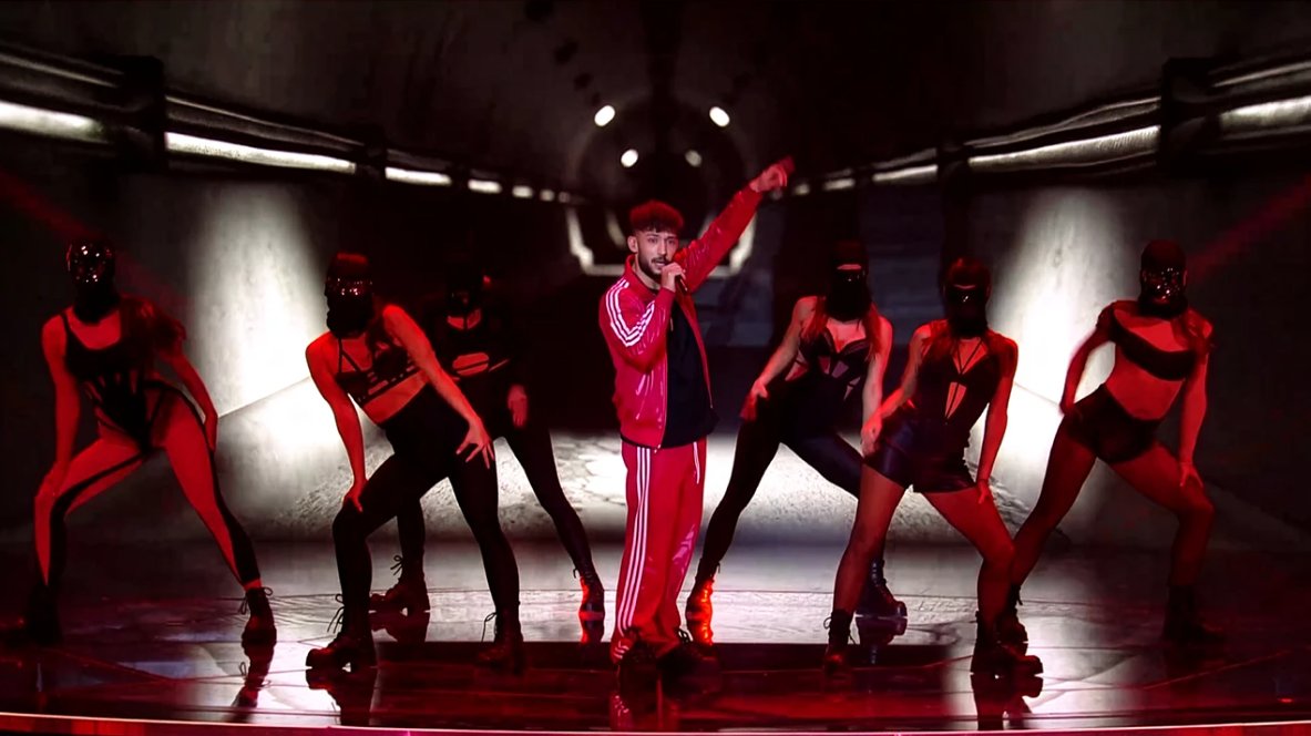 Performer with masked dancers under red stage lighting